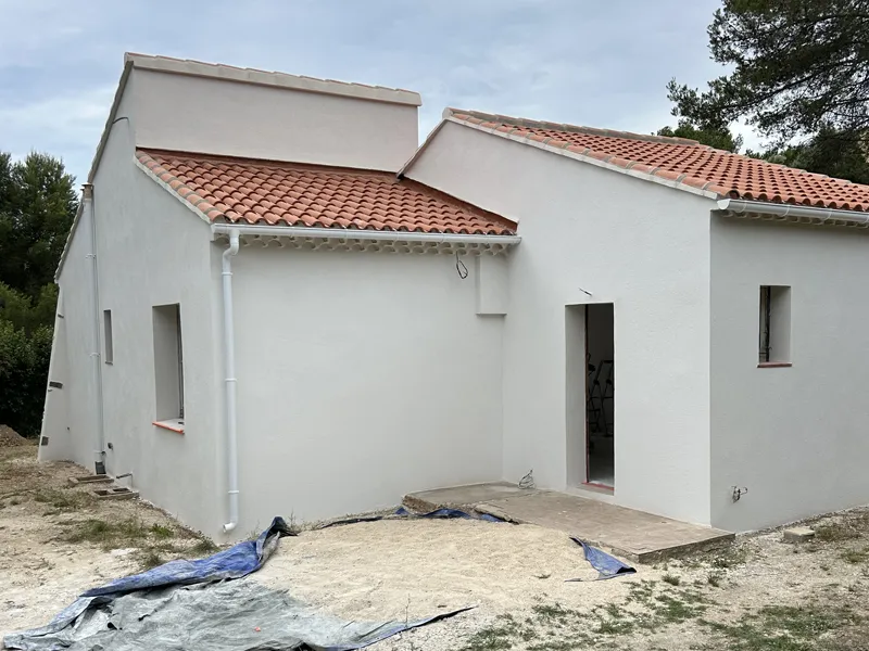 Maison terminée avec enduit blanc, gouttières et toiture en tuiles neuves